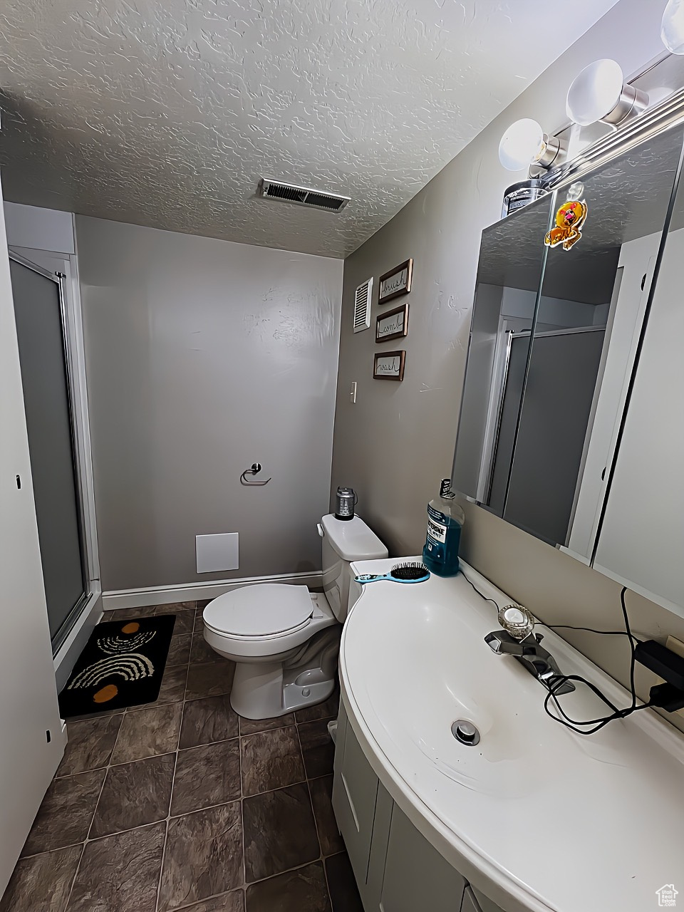 Bathroom featuring tile floors, vanity, a shower with shower door, toilet, and a textured ceiling