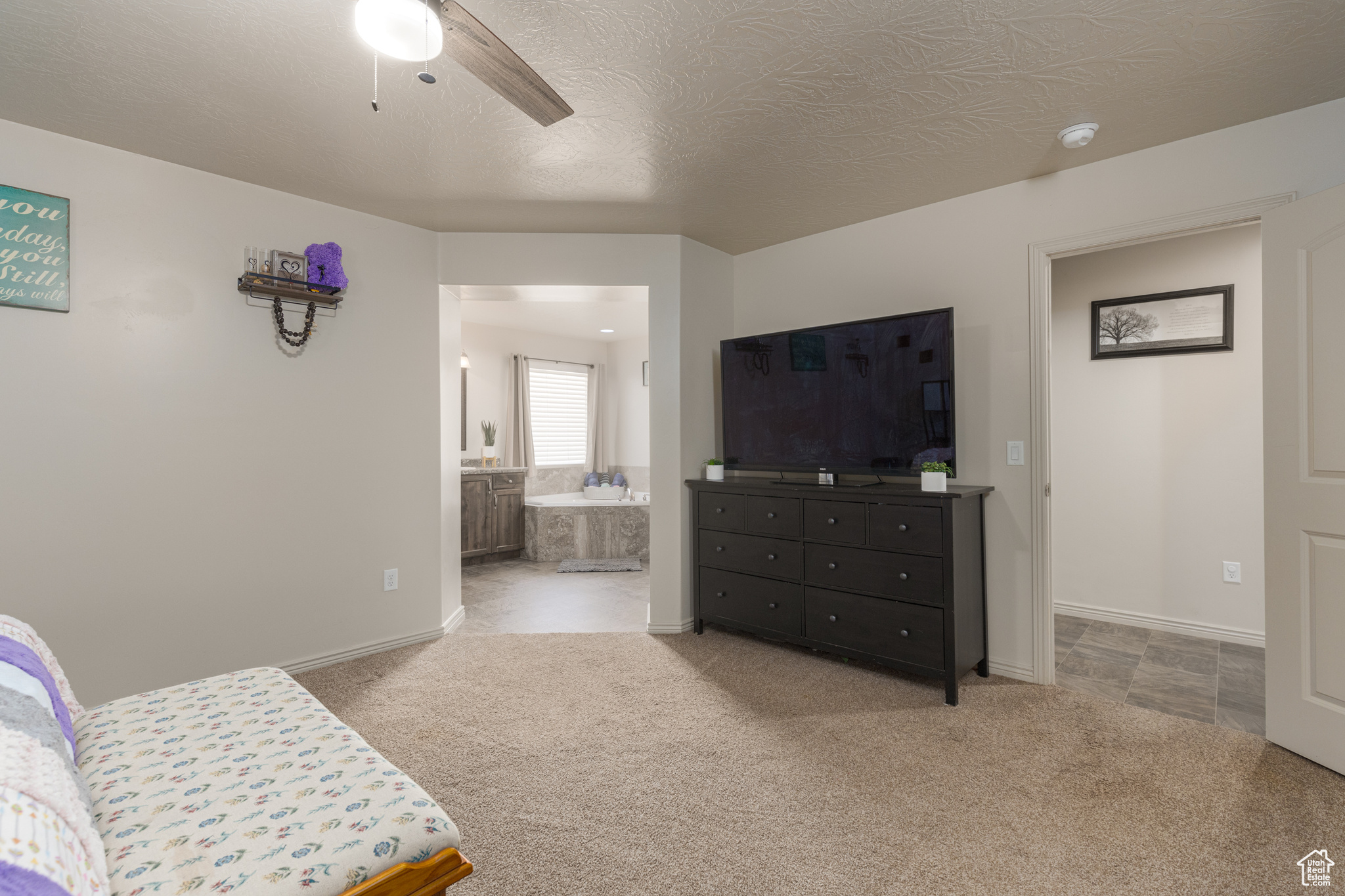 Tiled bedroom with ensuite bath, ceiling fan, and a textured ceiling