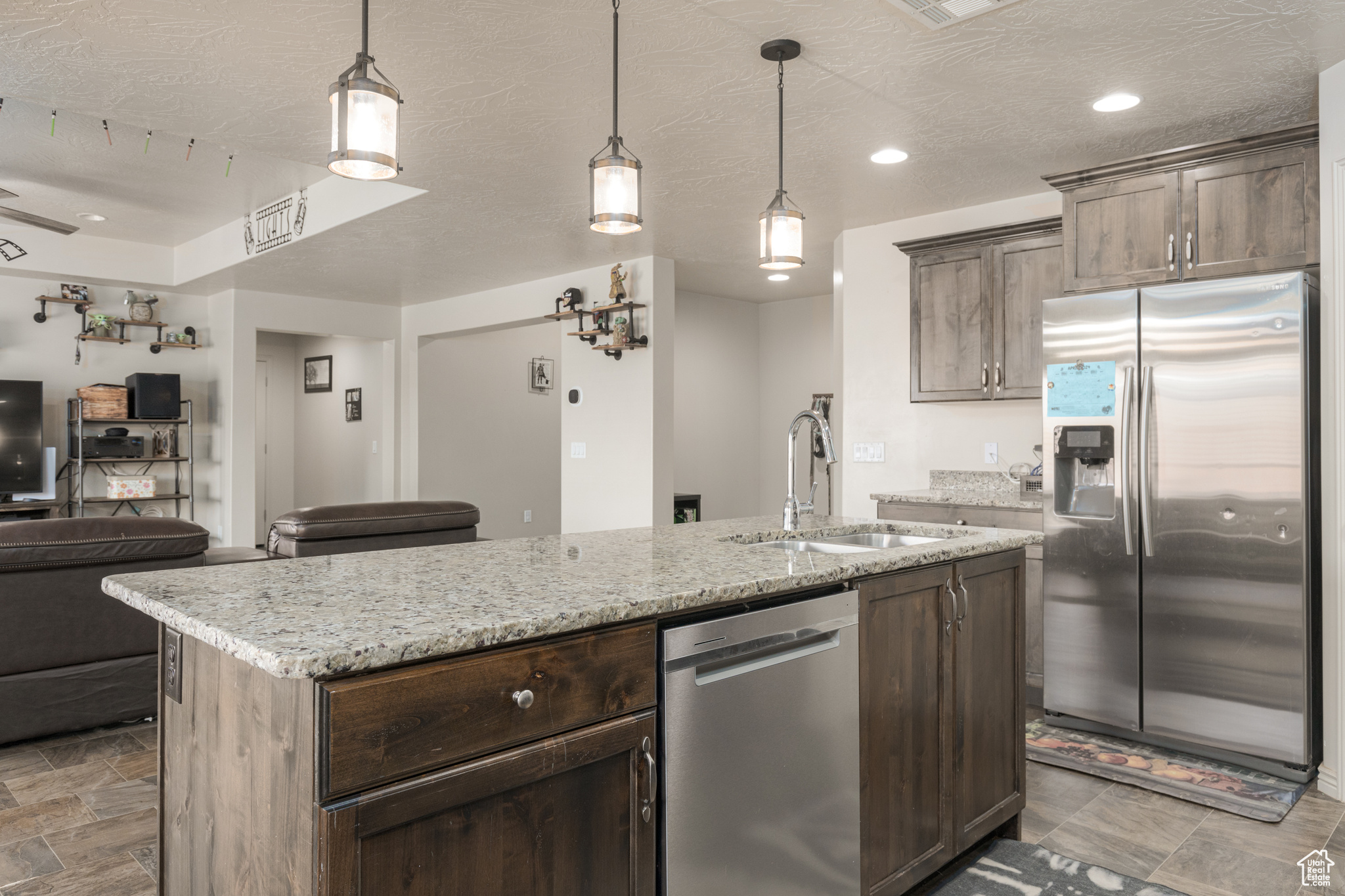 Kitchen featuring dark brown cabinets, appliances with stainless steel finishes, a center island with sink, tile flooring, and sink