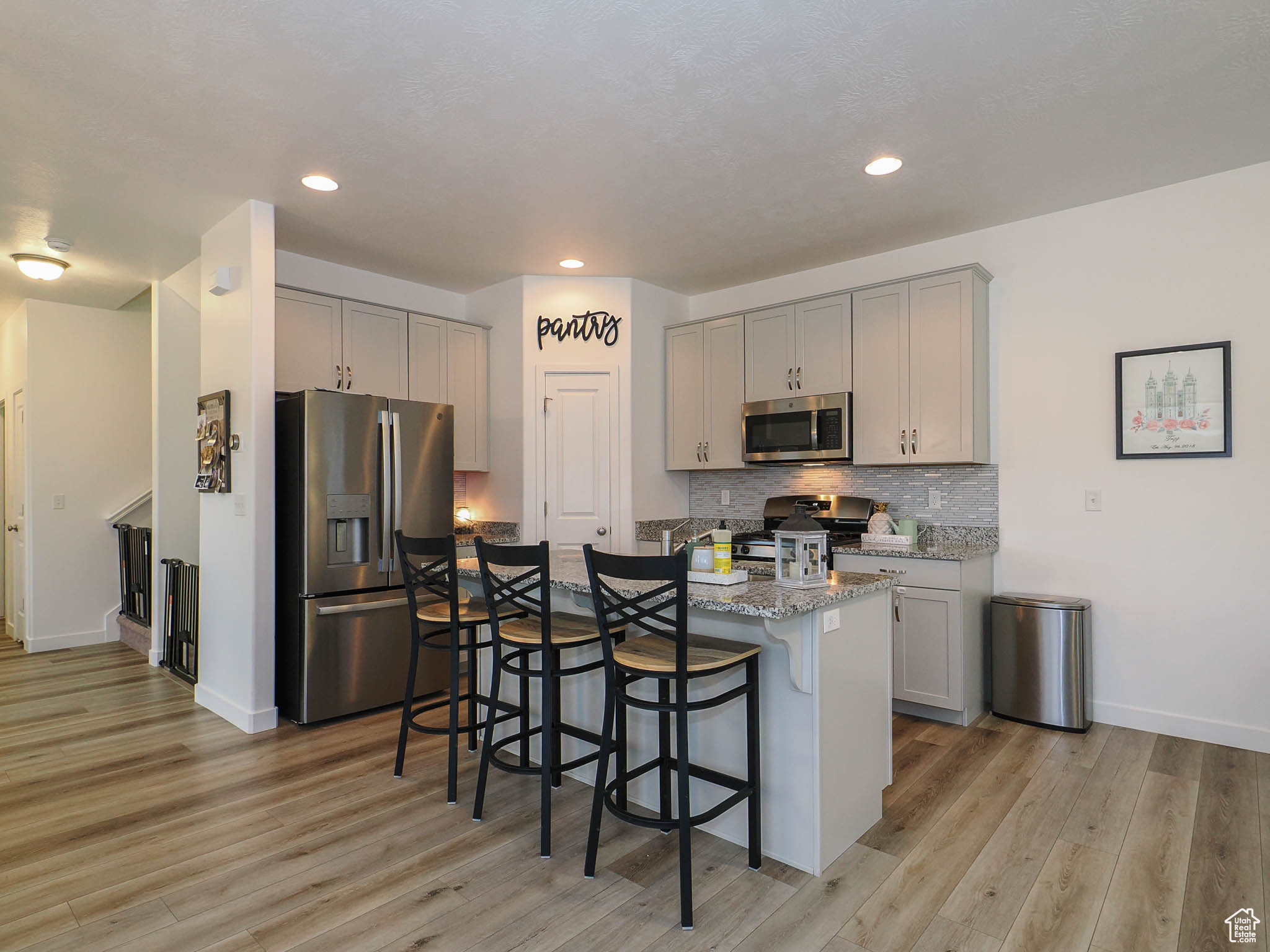 Kitchen with light hardwood / wood-style floors, gray cabinetry, stainless steel appliances, and a breakfast bar area