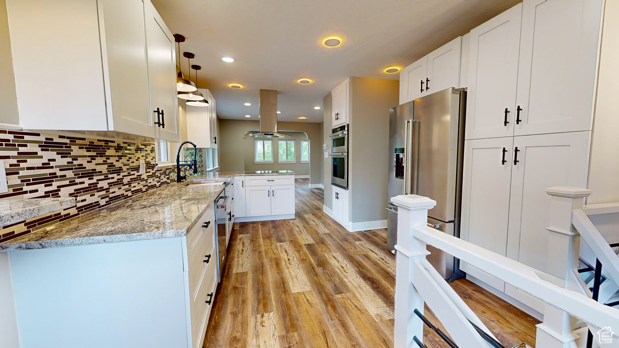 Kitchen with light wood-type flooring, hanging light fixtures, island exhaust hood, and white cabinetry