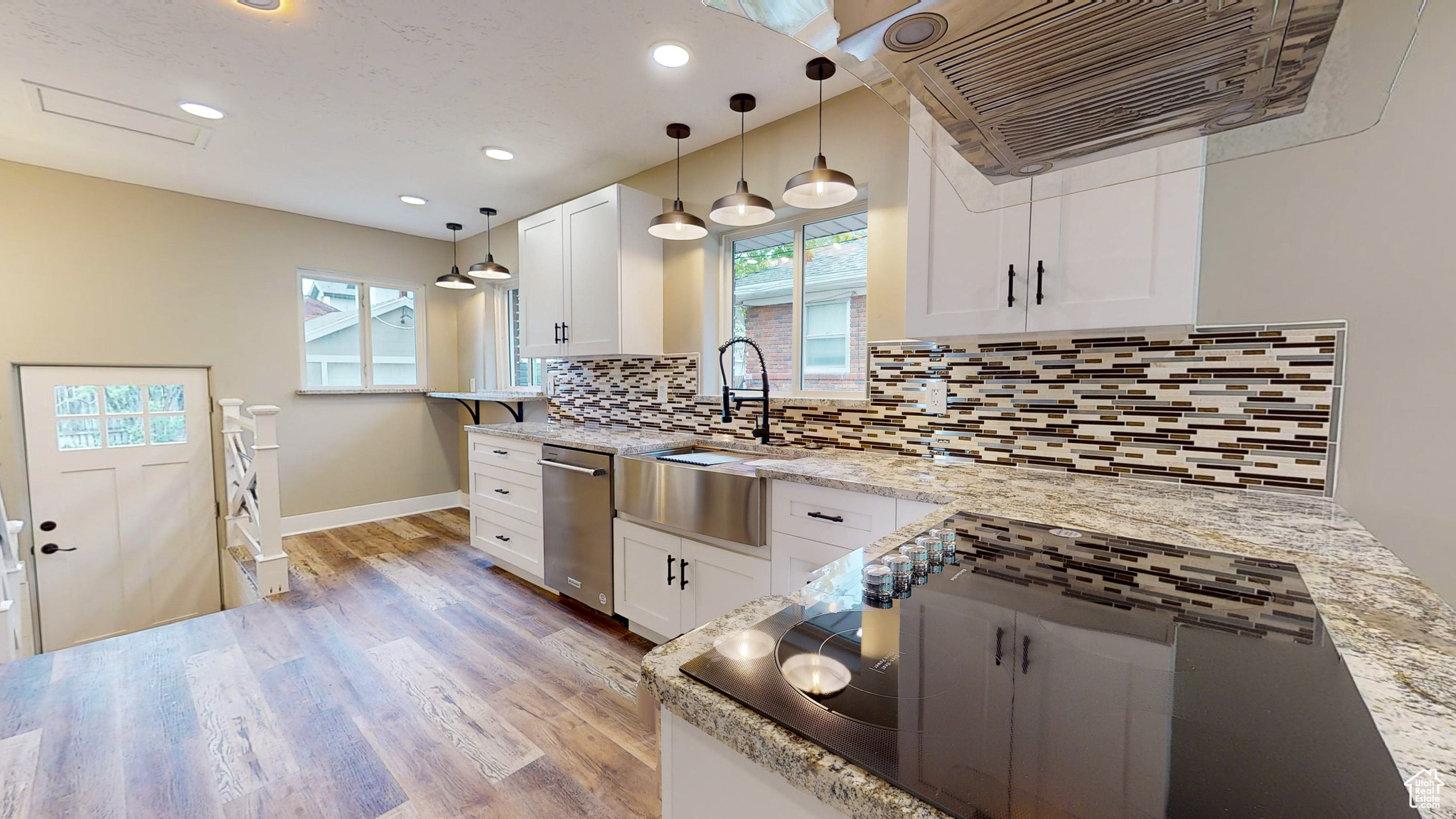 Kitchen featuring white cabinets, sink, dishwasher, backsplash, and hanging light fixtures