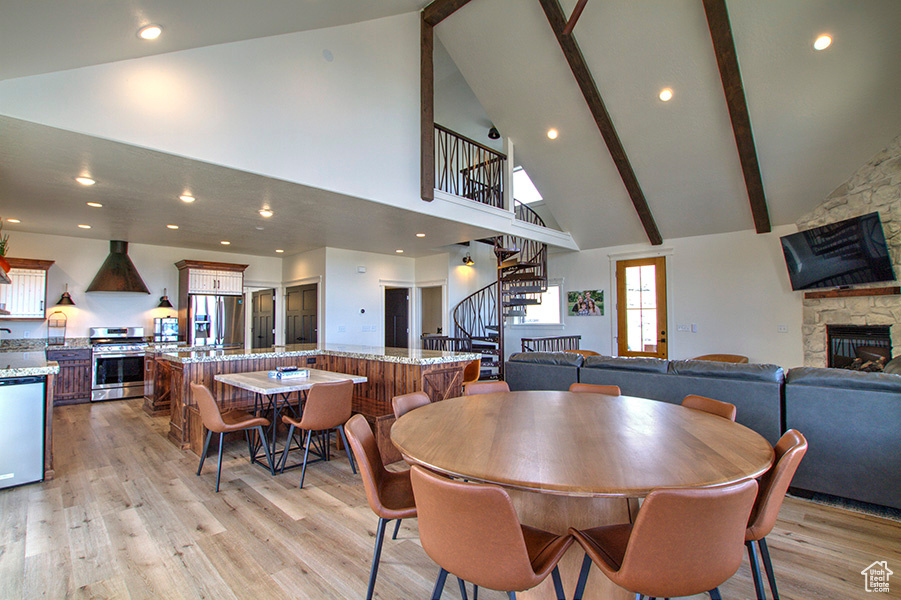 Dining room with a stone fireplace, light hardwood / wood-style flooring, beamed ceiling, and high vaulted ceiling