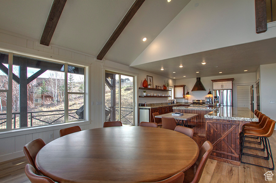 Dining space featuring high vaulted ceiling, light hardwood / wood-style flooring, and beamed ceiling