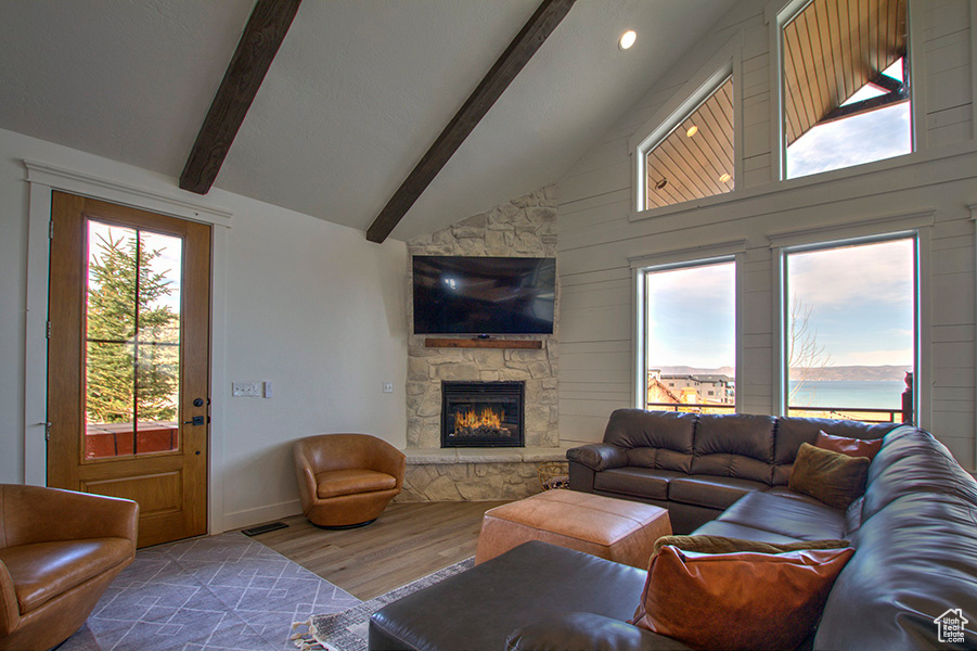 Living room with beamed ceiling, wood-type flooring, high vaulted ceiling, and a stone fireplace