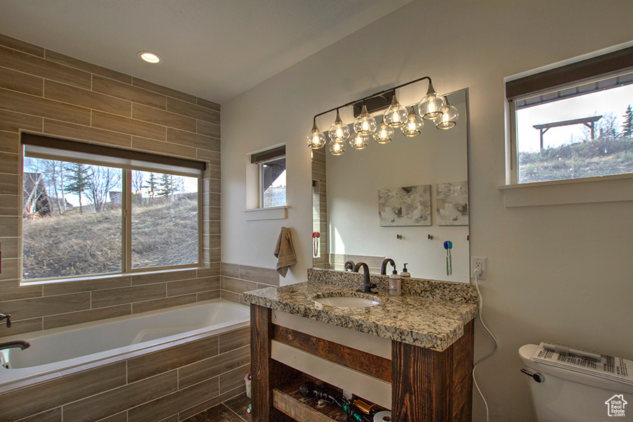 Bathroom with vanity with extensive cabinet space, toilet, and tiled bath