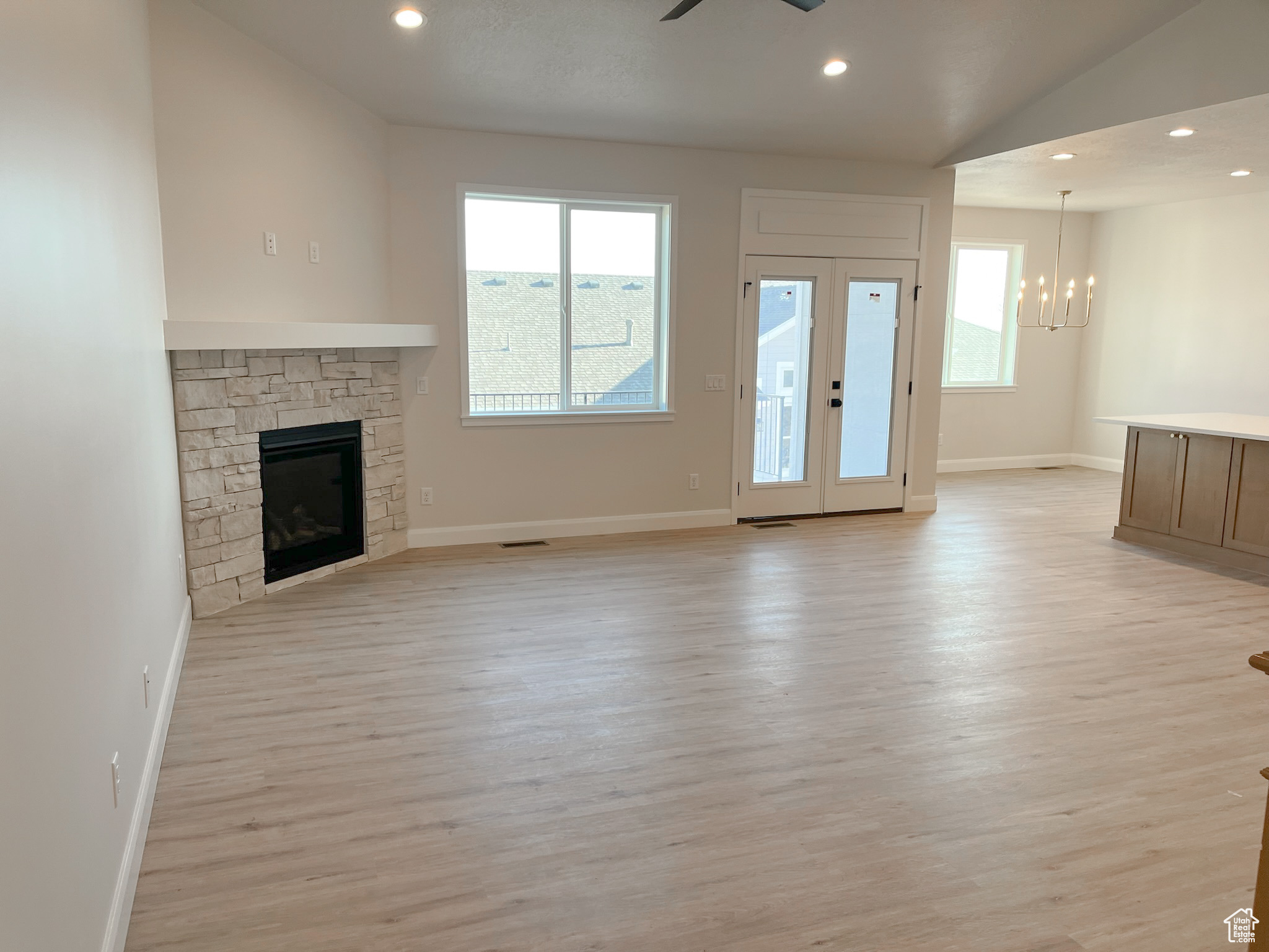 Unfurnished living room featuring light hardwood / wood-style floors, ceiling fan with notable chandelier, french doors, and a fireplace