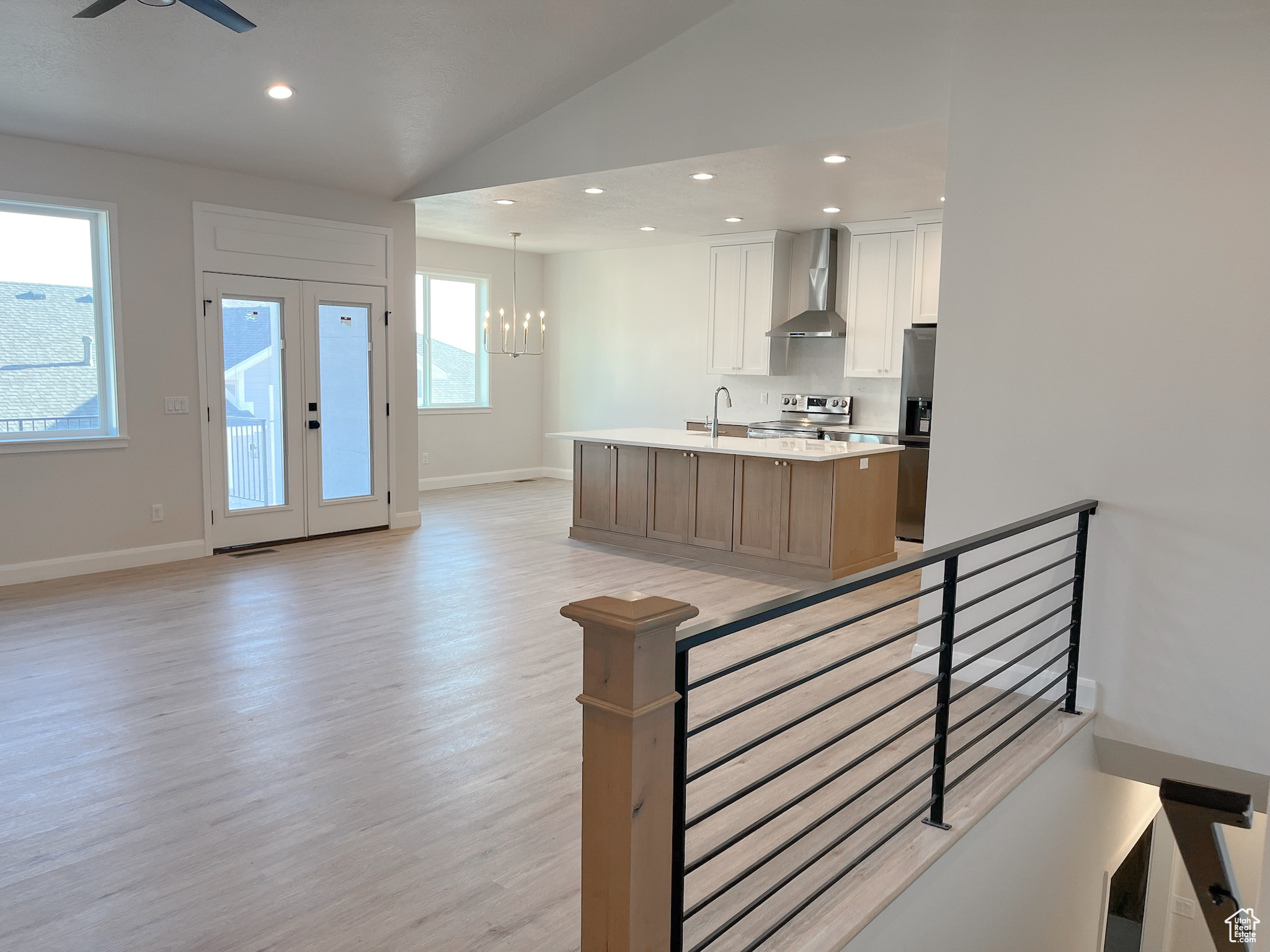 Kitchen featuring white cabinetry, an island with sink, light hardwood / wood-style flooring, wall chimney range hood, and ceiling fan with notable chandelier