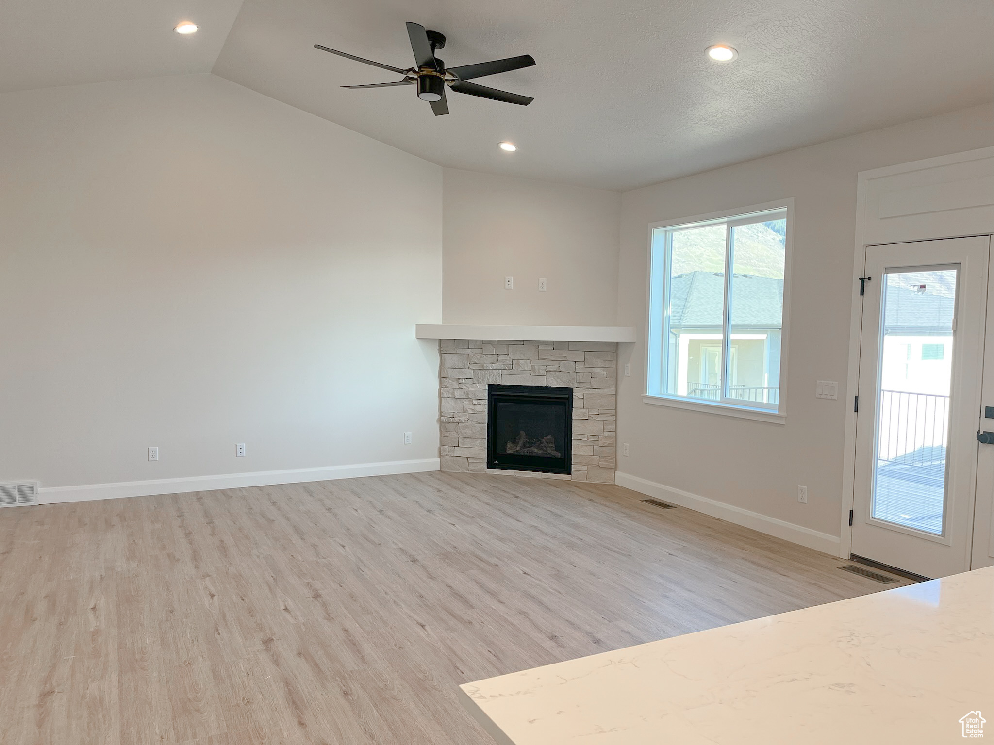 Unfurnished living room with lofted ceiling, ceiling fan, a stone fireplace, and light hardwood / wood-style flooring