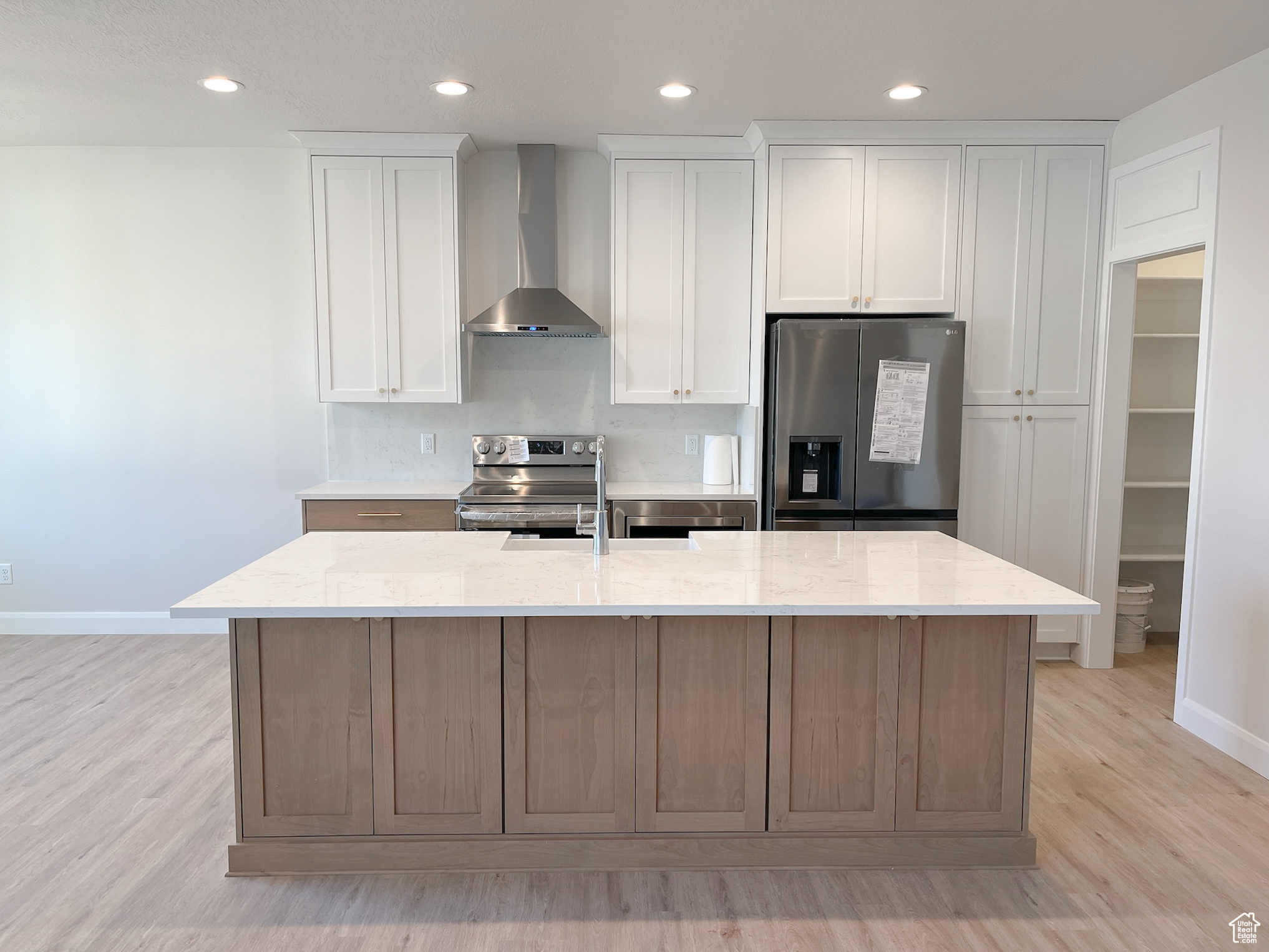 Kitchen with wall chimney exhaust hood, a kitchen island with sink, appliances with stainless steel finishes, and light wood-type flooring