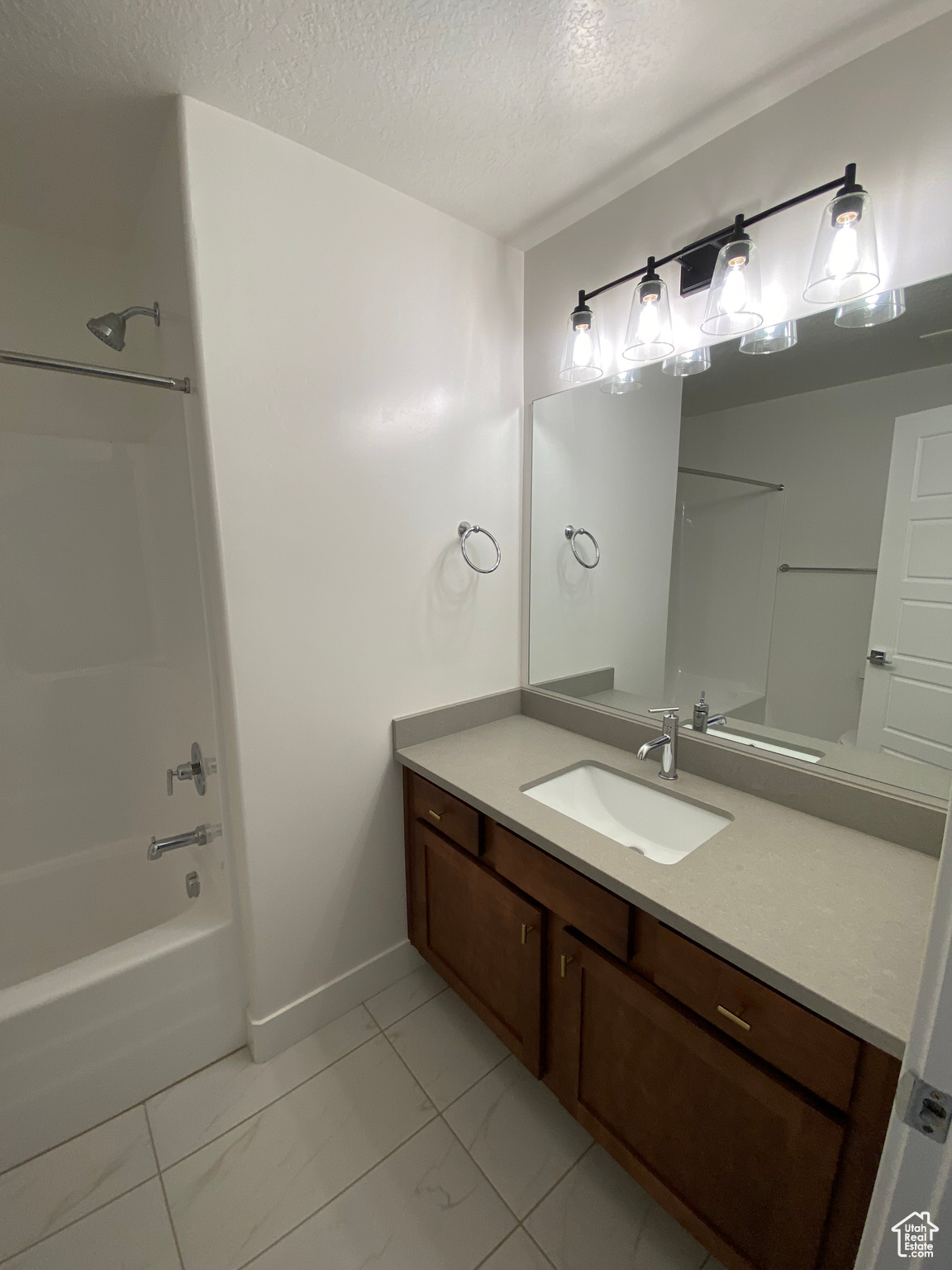 Bathroom with washtub / shower combination, vanity, tile floors, and a textured ceiling
