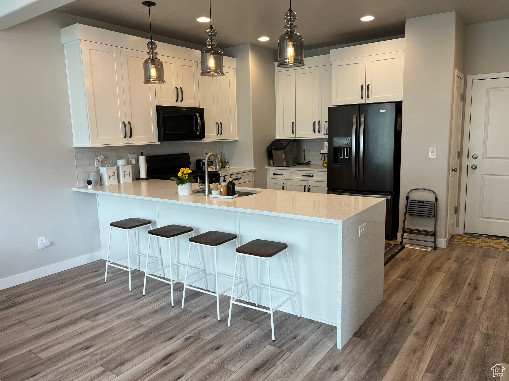 Kitchen featuring backsplash, appliances, wood-type flooring, white cabinets, and sink