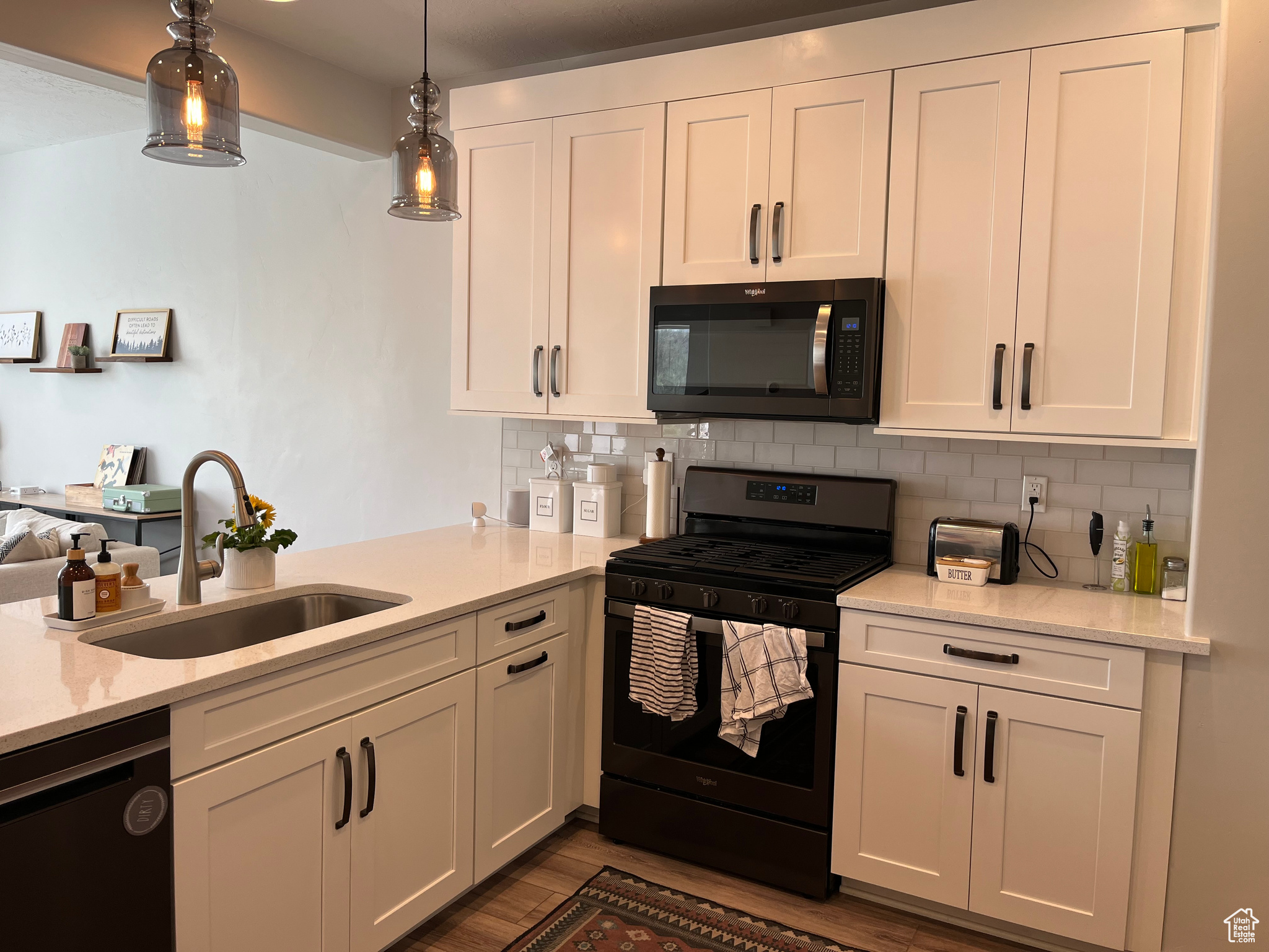 Kitchen with hanging light fixtures, dark hardwood / wood-style flooring, black appliances, backsplash, and sink