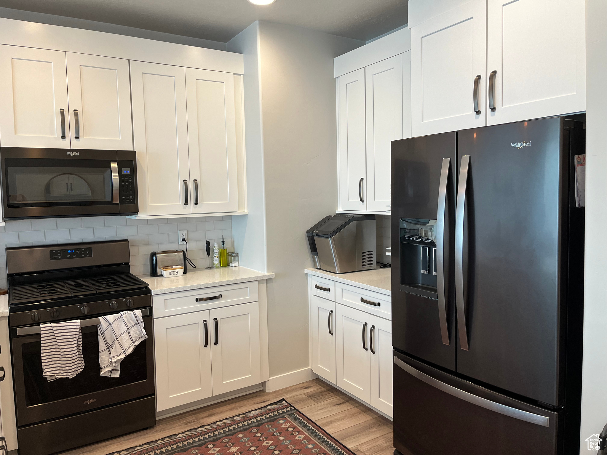 Kitchen featuring backsplash, stainless steel appliances, light hardwood / wood-style floors, and white cabinets