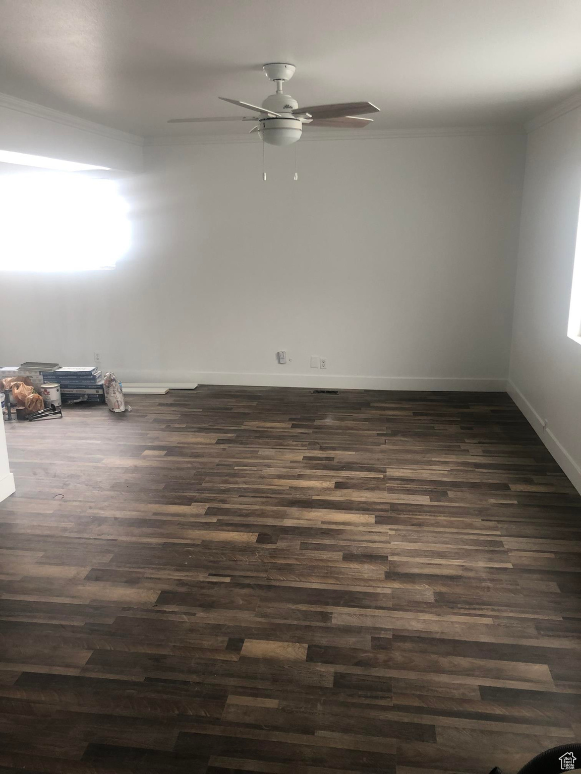 Empty room featuring a healthy amount of sunlight, ceiling fan, dark wood-type flooring, and crown molding