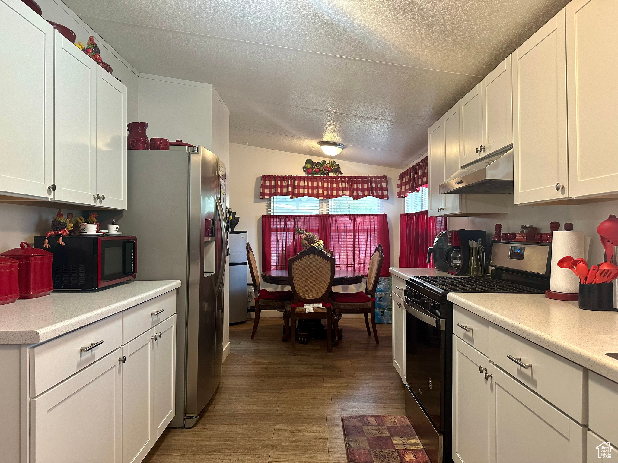 Kitchen with a textured ceiling, gas range, white cabinets, lofted ceiling, and wood-type flooring