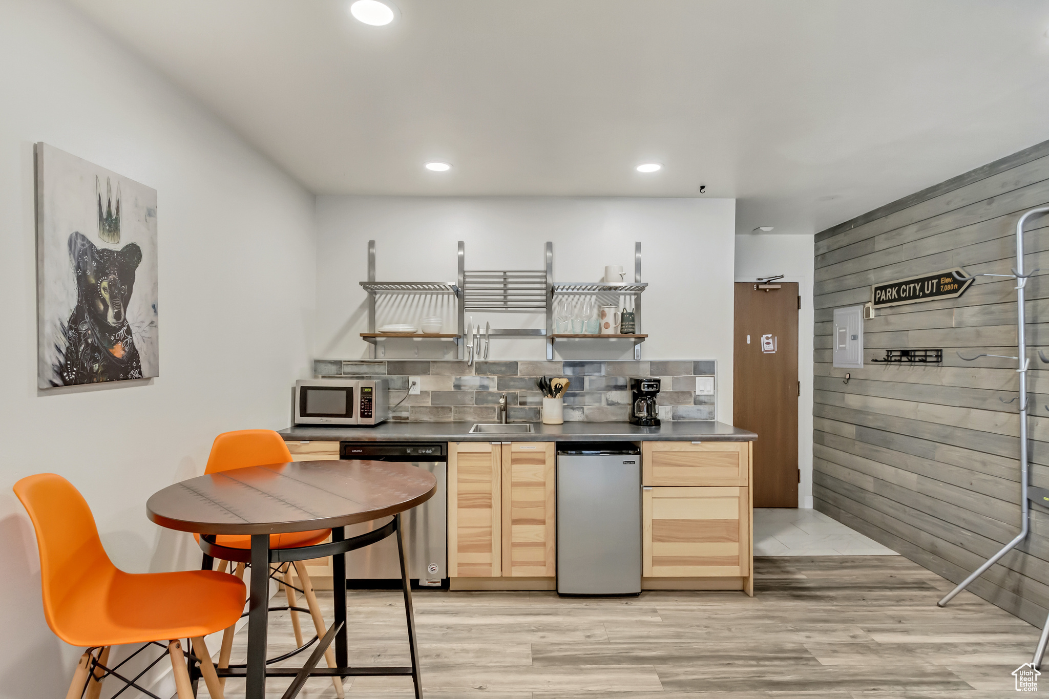 Kitchen with light wood-type flooring, light brown cabinetry, backsplash, wood walls, and appliances with stainless steel finishes