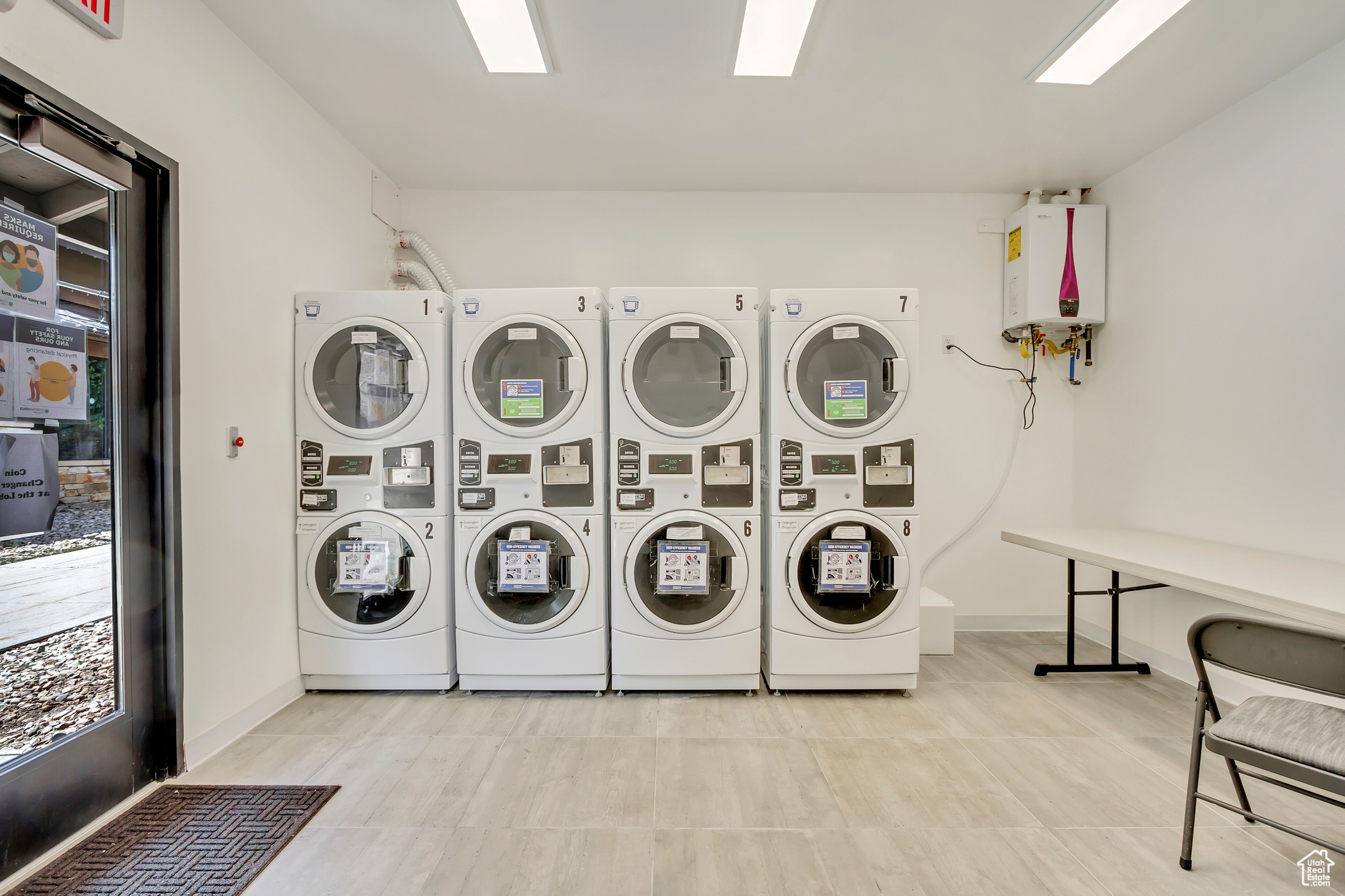 Clothes washing area with light tile flooring, tankless water heater, stacked washer / drying machine, and washing machine and clothes dryer