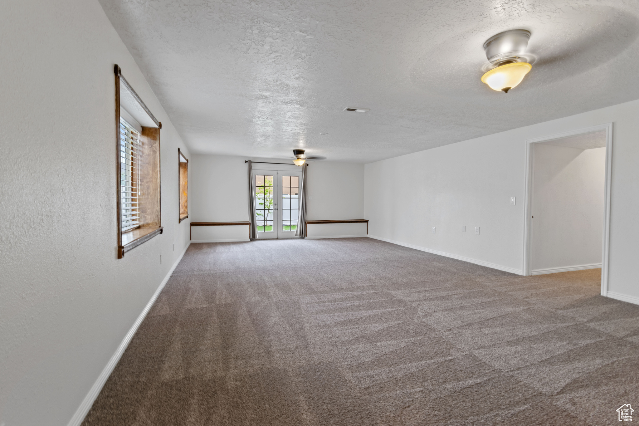 Empty room featuring a textured ceiling, carpet floors, and ceiling fan