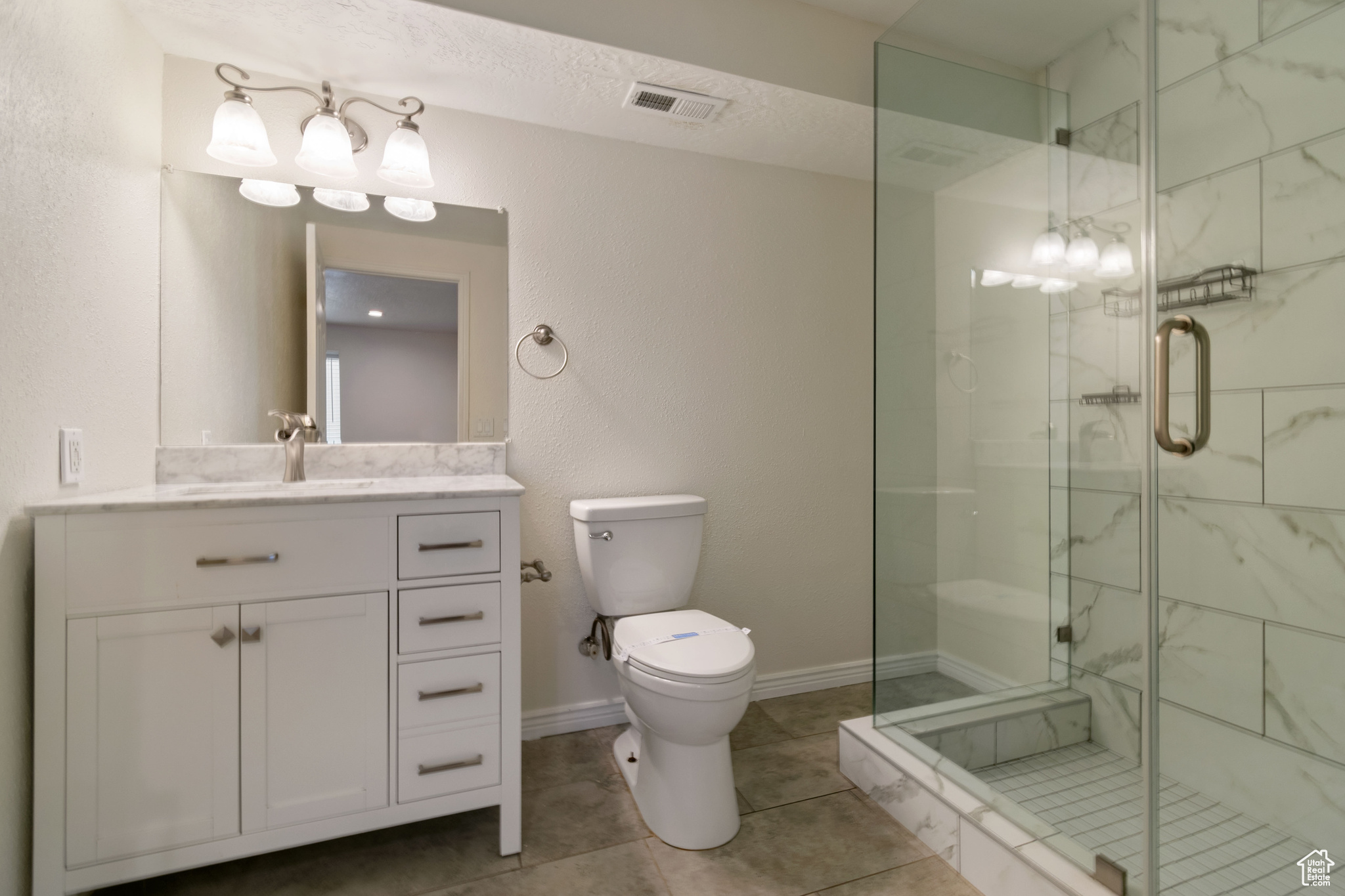 Bathroom with a textured ceiling, tile floors, toilet, a shower with shower door, and vanity