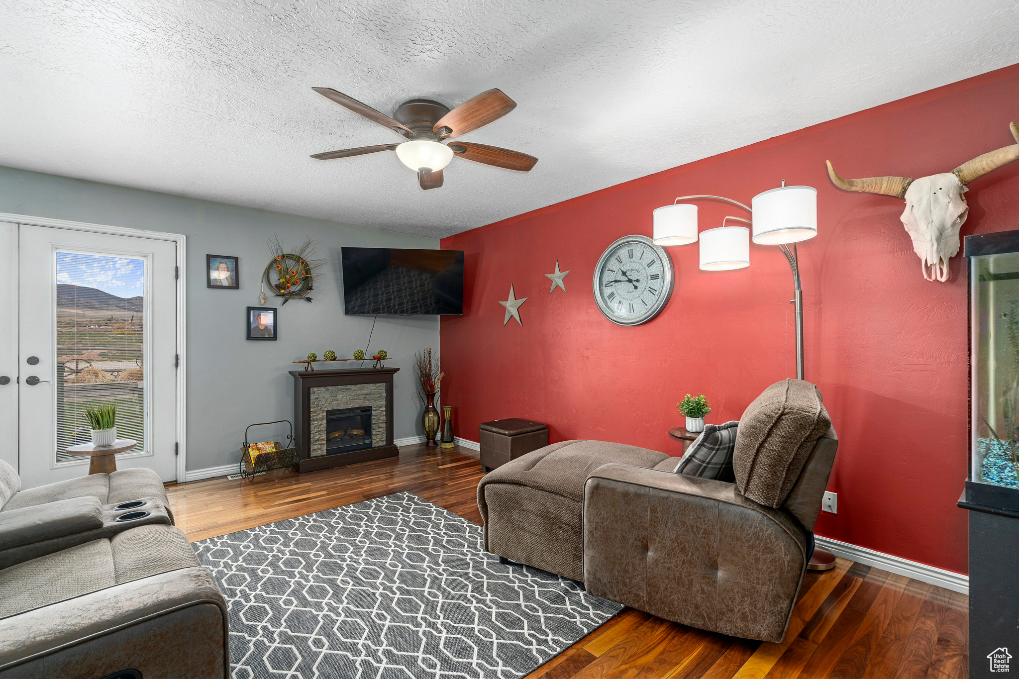 Living room featuring ceiling fan, a stone fireplace, a textured ceiling, dark wood flooring, and french doors