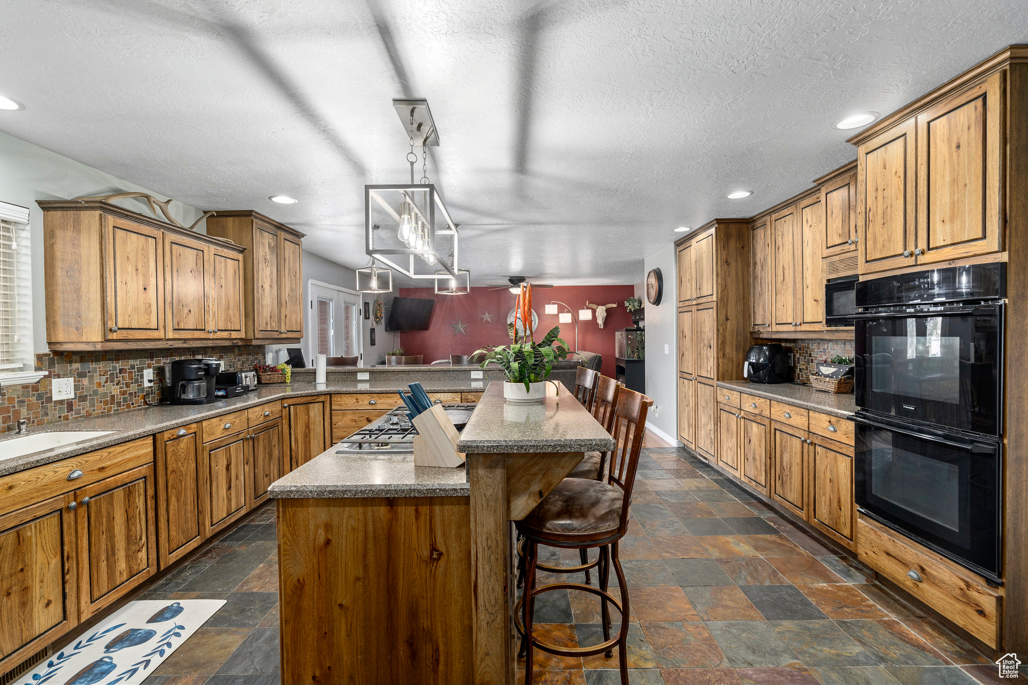 Kitchen featuring black appliances, backsplash, a kitchen bar, a kitchen island, and dark tile flooring