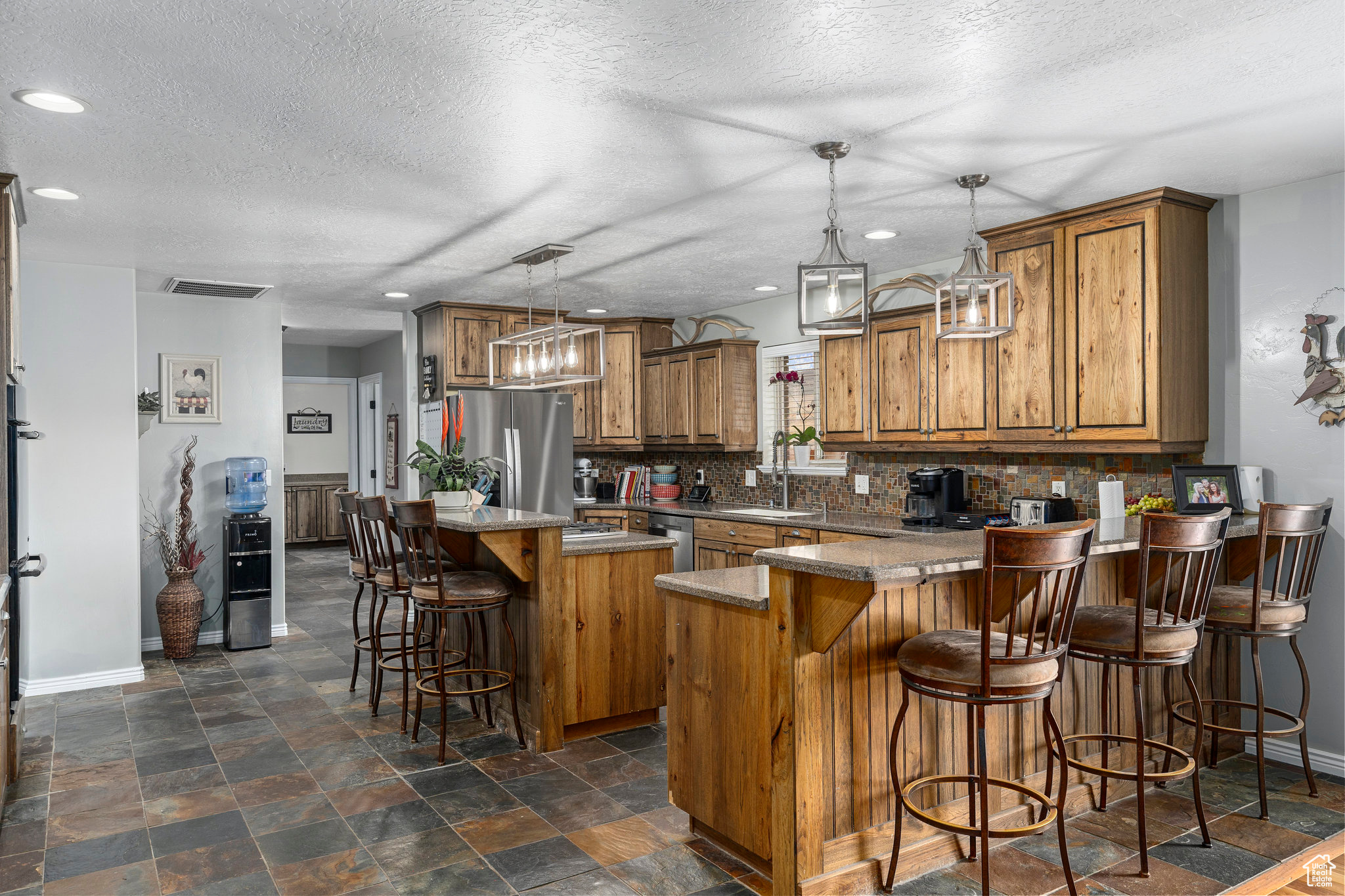 Kitchen with dark tile floors, pendant lighting, backsplash, appliances with stainless steel finishes, and a kitchen bar