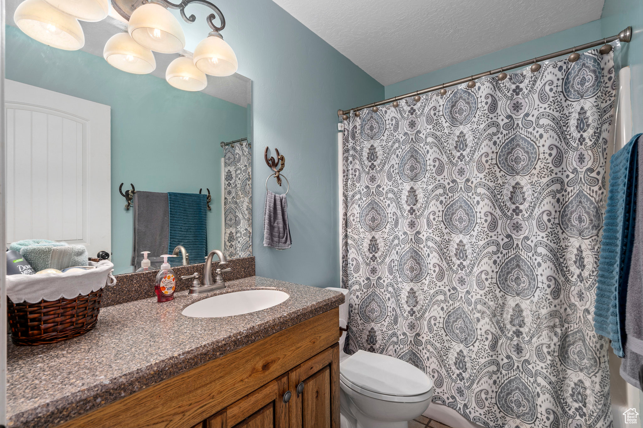 Bathroom with a chandelier, vanity with extensive cabinet space, toilet, and a textured ceiling