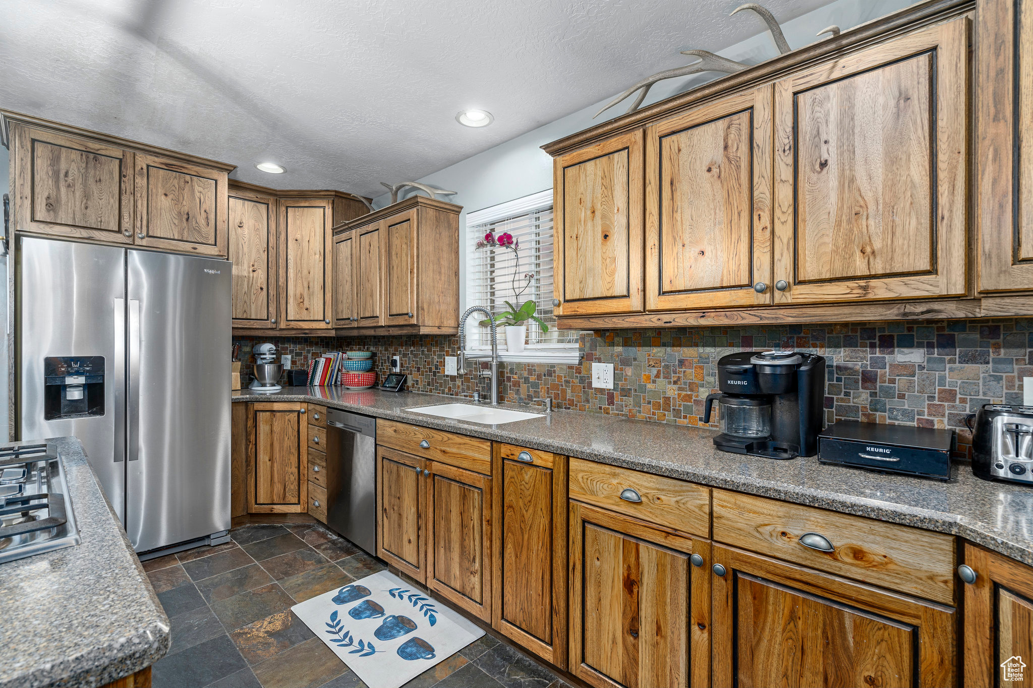 Kitchen with sink, dark tile flooring, tasteful backsplash, and stainless steel appliances