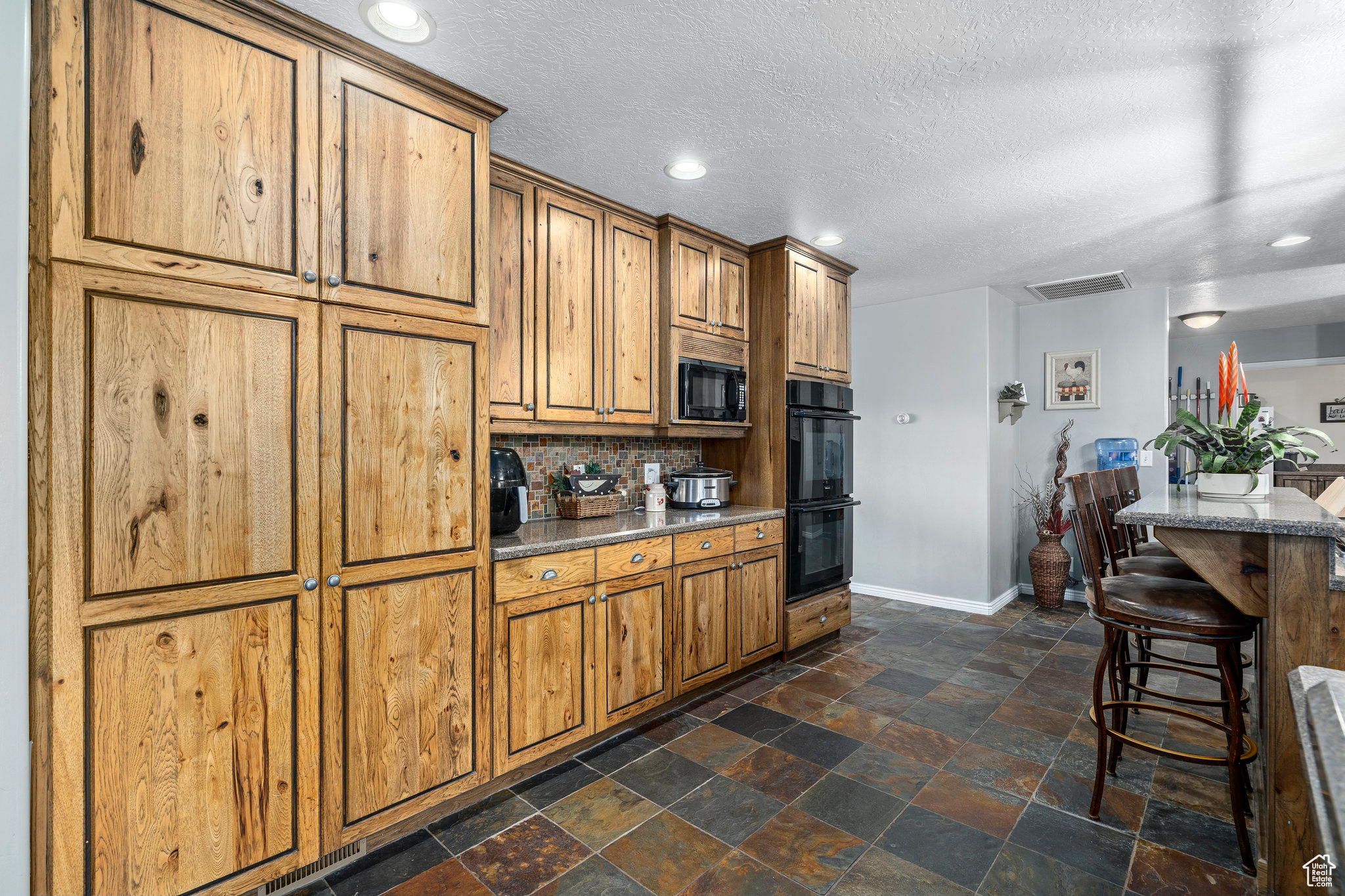 Kitchen featuring backsplash, black appliances, a textured ceiling, a breakfast bar, and dark tile floors