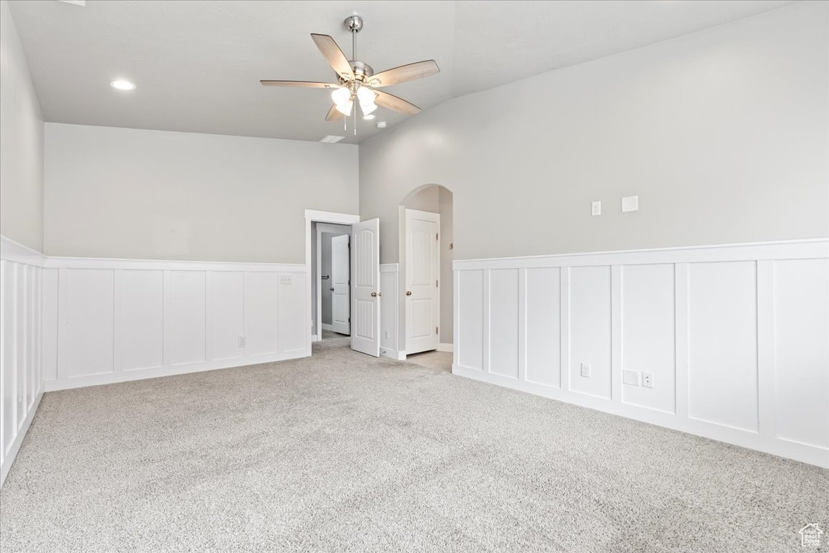 Carpeted spare room with ceiling fan and high vaulted ceiling