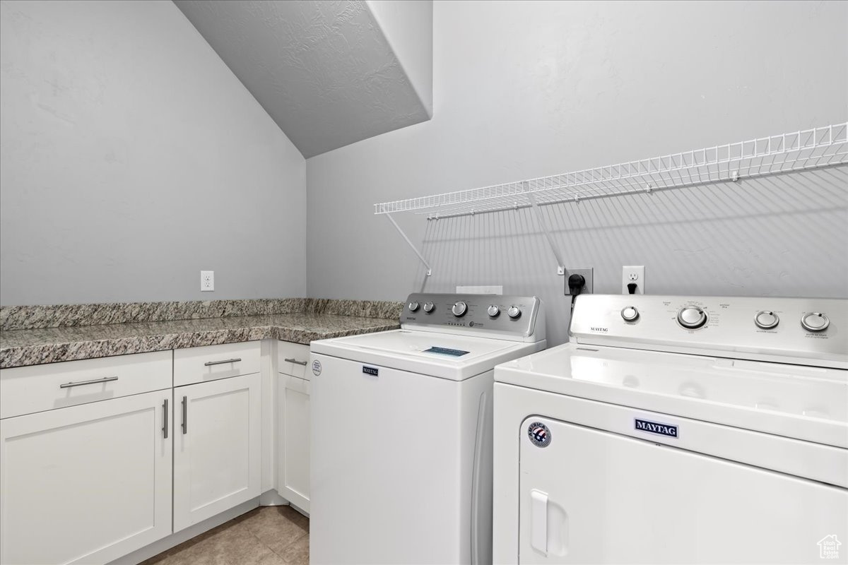 Clothes washing area featuring electric dryer hookup, cabinets, light tile floors, and washing machine and clothes dryer