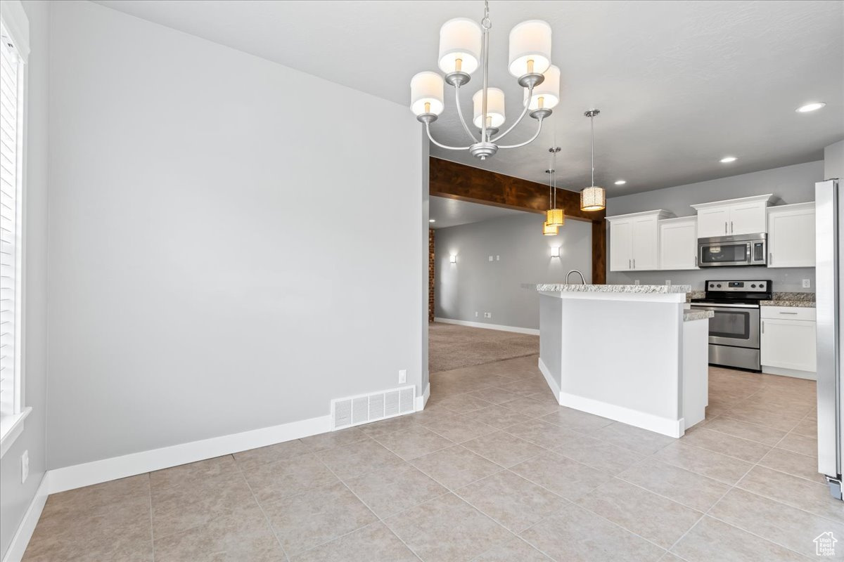 Kitchen featuring light stone counters, a notable chandelier, light tile flooring, hanging light fixtures, and stainless steel appliances