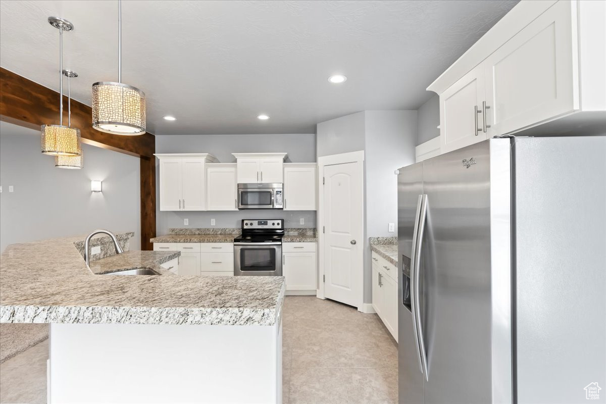 Kitchen with appliances with stainless steel finishes, sink, white cabinets, and hanging light fixtures