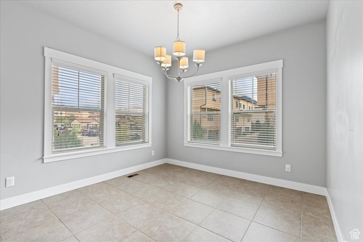 Empty room with light tile flooring and an inviting chandelier