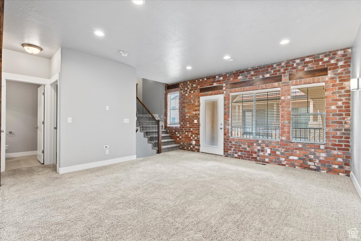 Carpeted empty room featuring brick wall