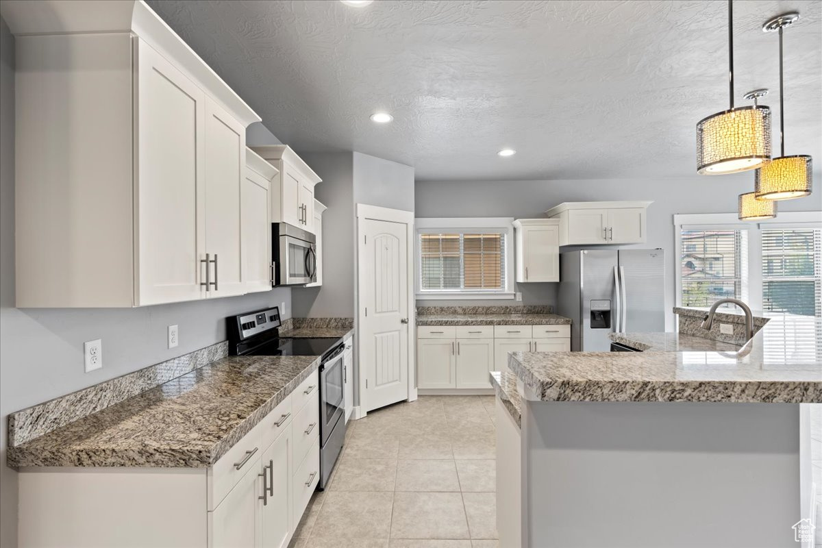 Kitchen featuring white cabinets, stainless steel appliances, light tile floors, and a healthy amount of sunlight