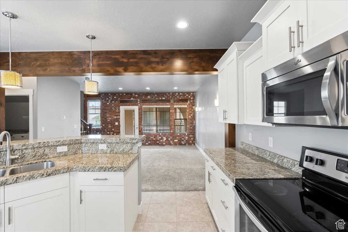 Kitchen featuring brick wall, stainless steel appliances, decorative light fixtures, and beam ceiling