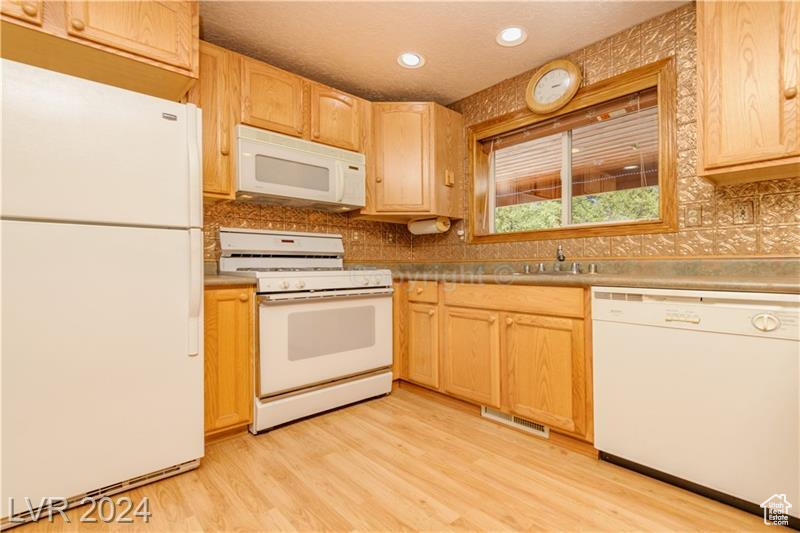 Kitchen with backsplash, light hardwood / wood-style flooring, light brown cabinets, and white appliances