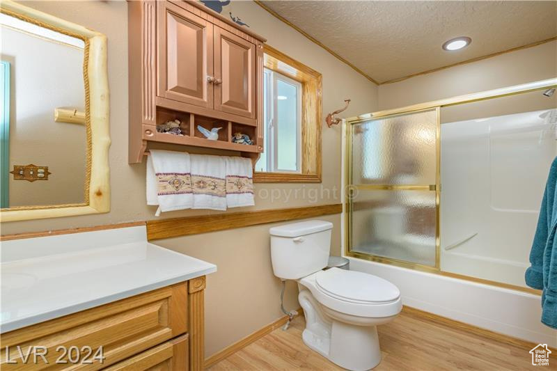 Full bathroom featuring wood-type flooring, shower / bath combination with glass door, vanity, toilet, and a textured ceiling