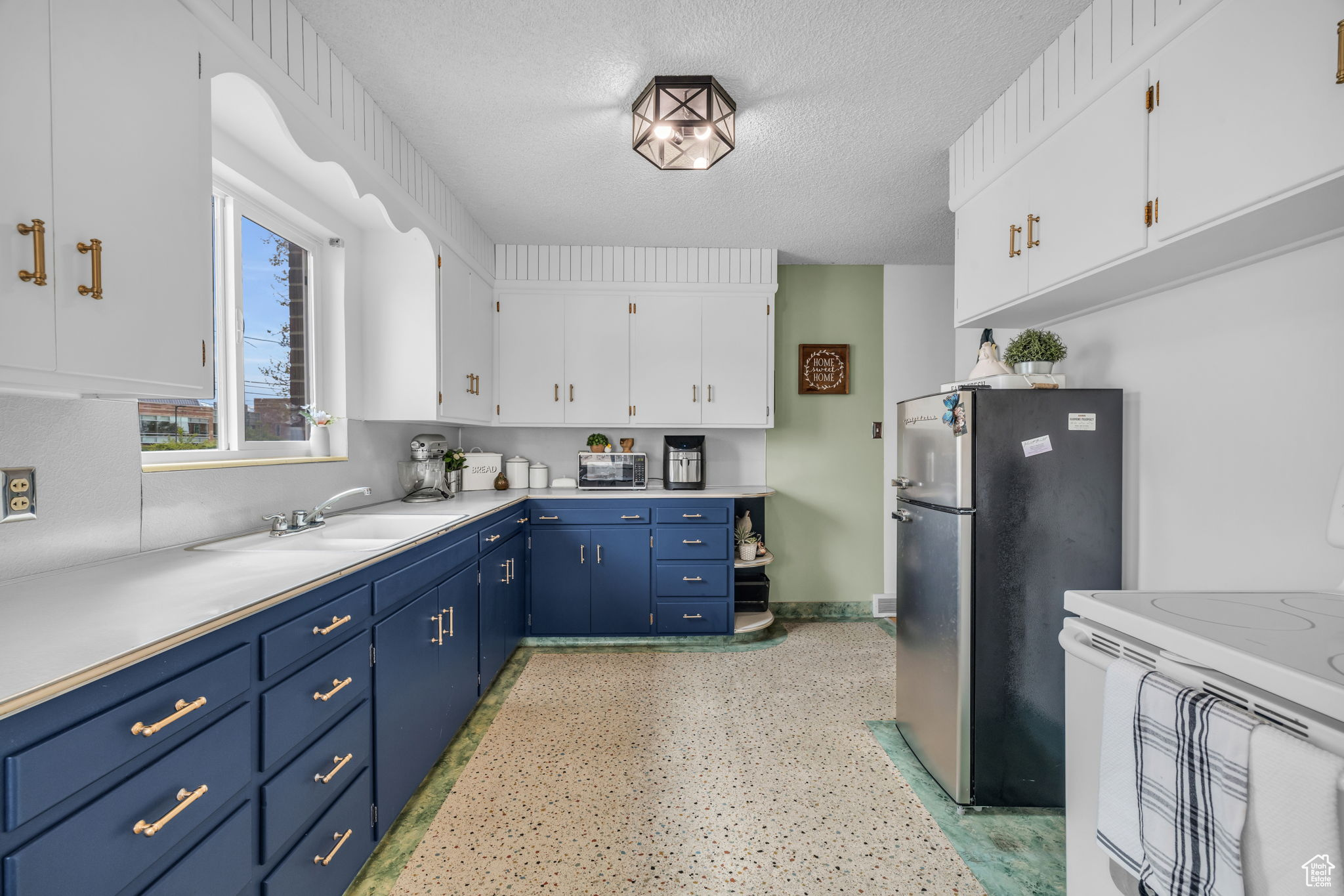 Kitchen with a textured ceiling, stainless steel refrigerator, white cabinetry, blue cabinetry, and white range oven