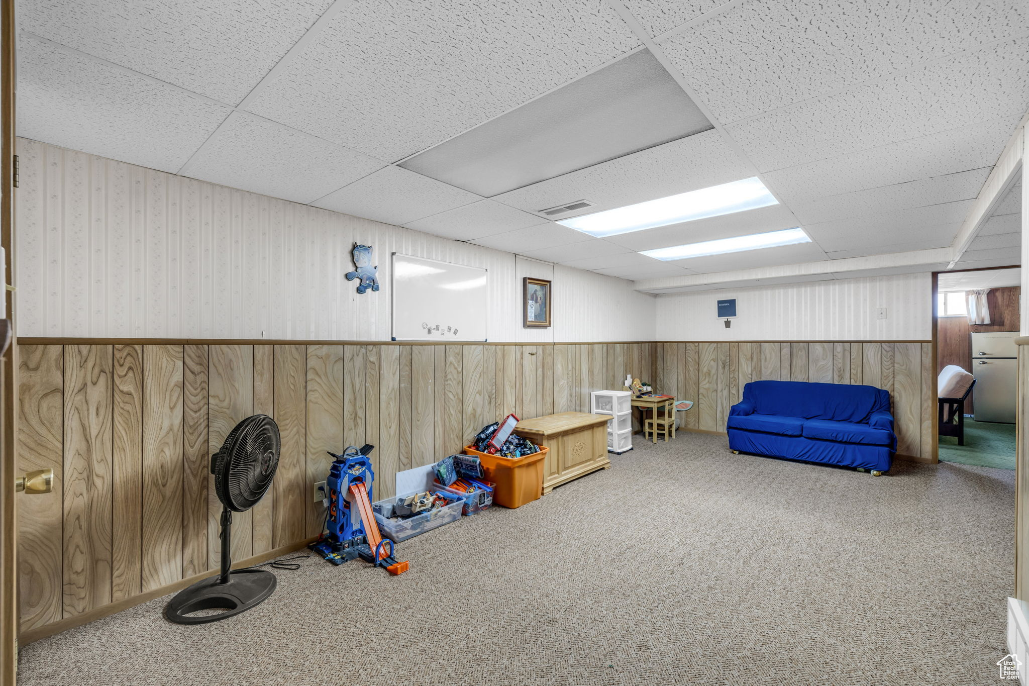 Playroom with a paneled ceiling, carpet flooring, and wooden walls