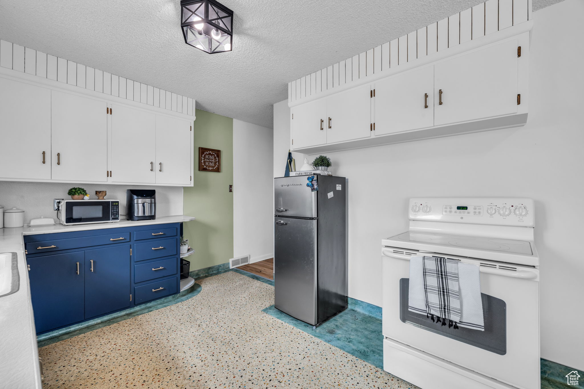 Kitchen featuring blue cabinets, white range with electric cooktop, a textured ceiling, white cabinets, and stainless steel refrigerator