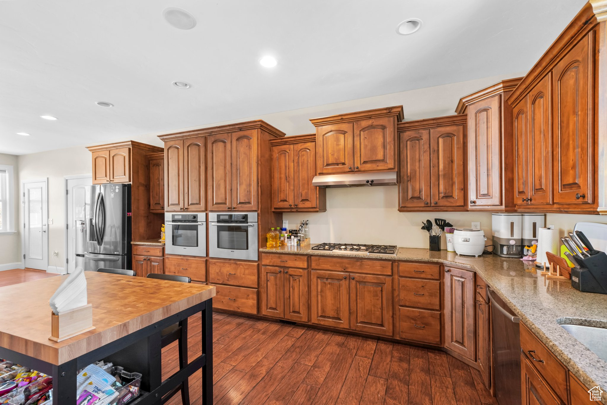 Kitchen featuring dark hardwood / wood-style flooring, appliances with stainless steel finishes, and light stone countertops