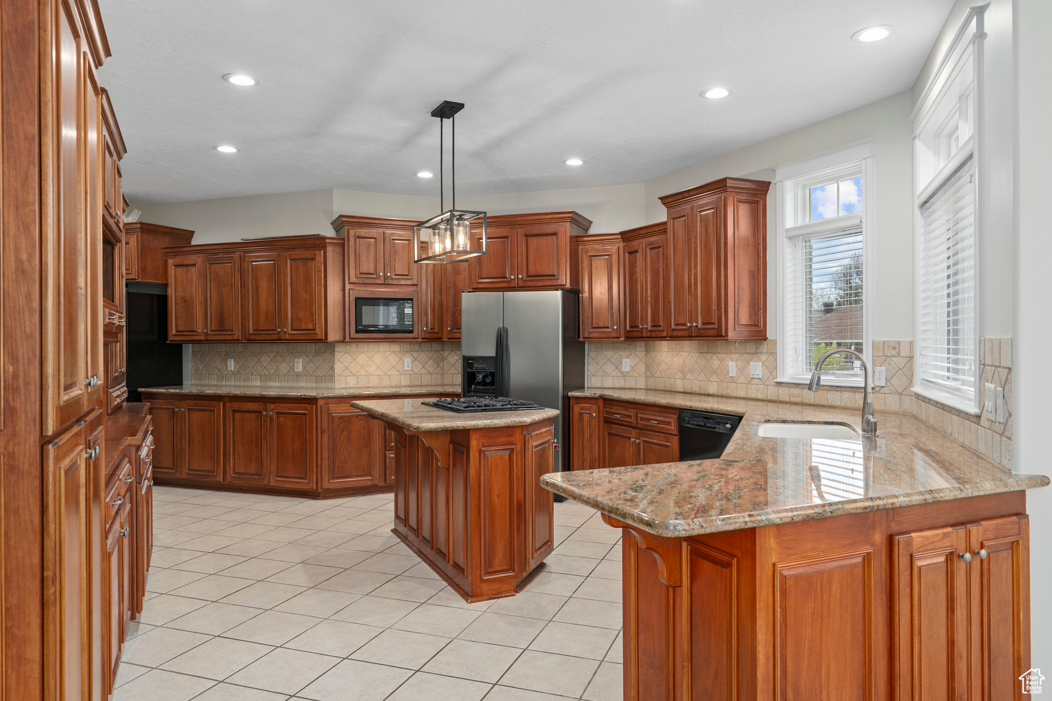 Kitchen with hanging light fixtures, a kitchen island, black appliances, tasteful backsplash, and sink