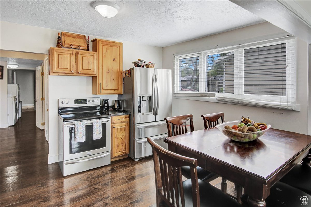 Kitchen with a textured ceiling, appliances with stainless steel finishes, light brown cabinetry, and dark wood-type flooring