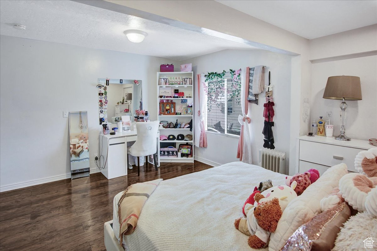 Bedroom with dark hardwood / wood-style flooring and radiator heating unit