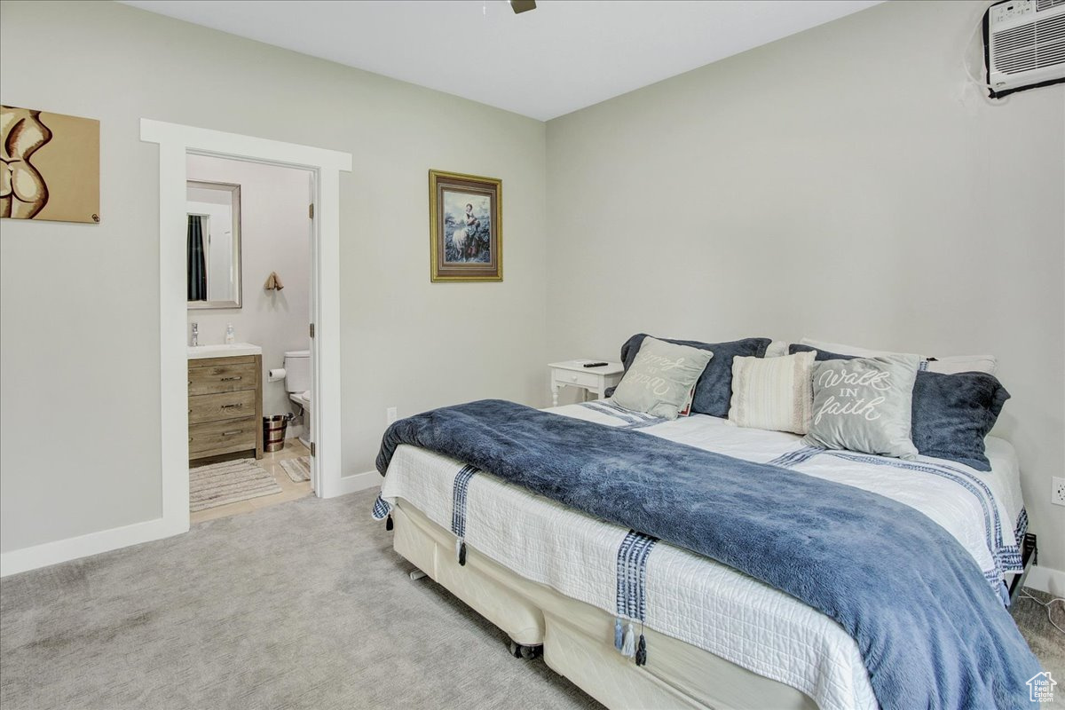 Carpeted bedroom featuring ceiling fan, ensuite bathroom, and a wall mounted AC