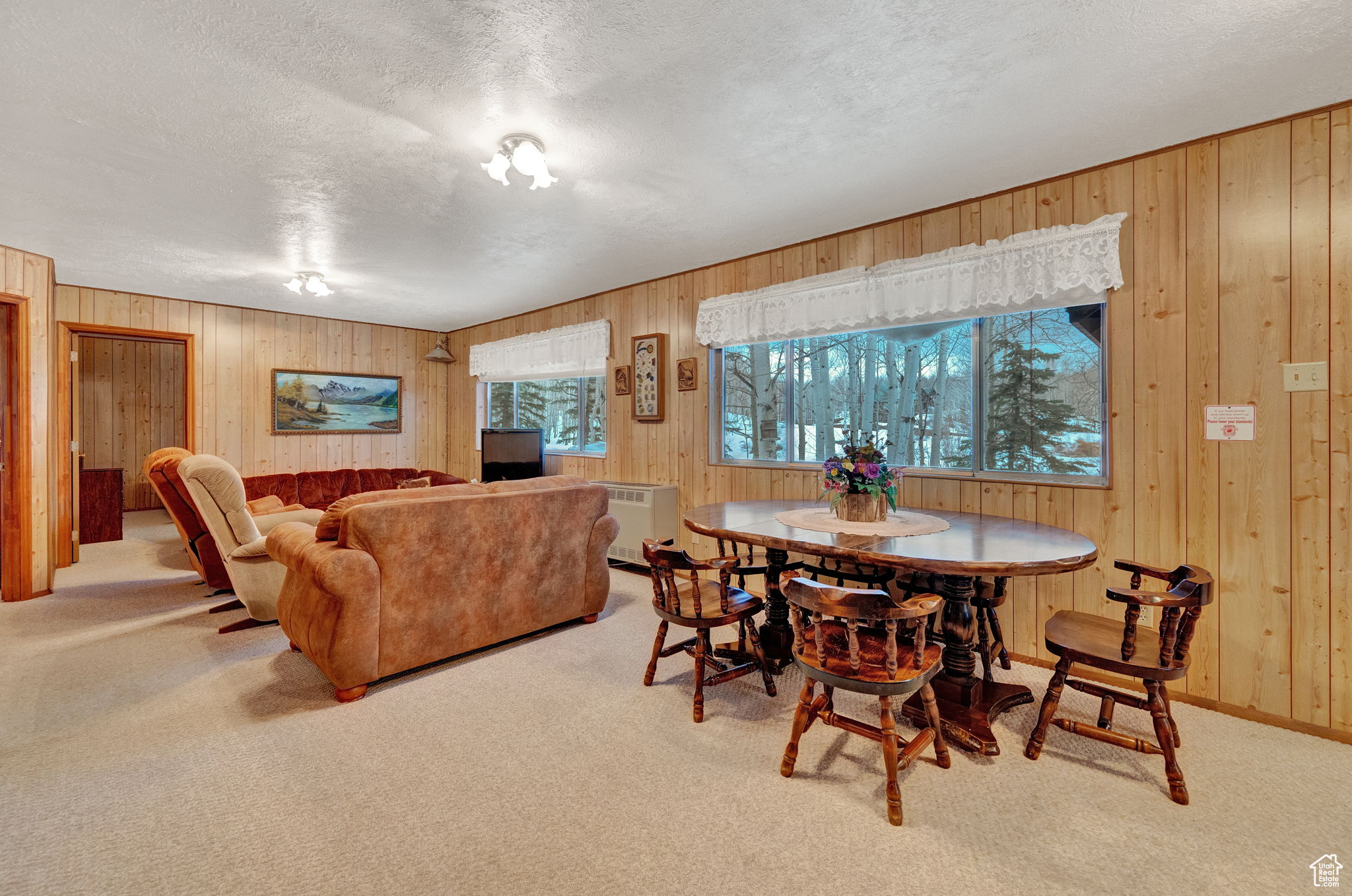 Dining room with a textured ceiling, wood walls, and light carpet