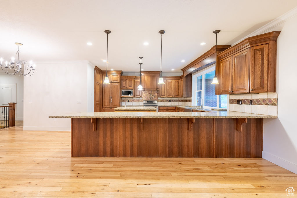 Kitchen with tasteful backsplash, stainless steel microwave, light hardwood / wood-style flooring, pendant lighting, and light stone countertops